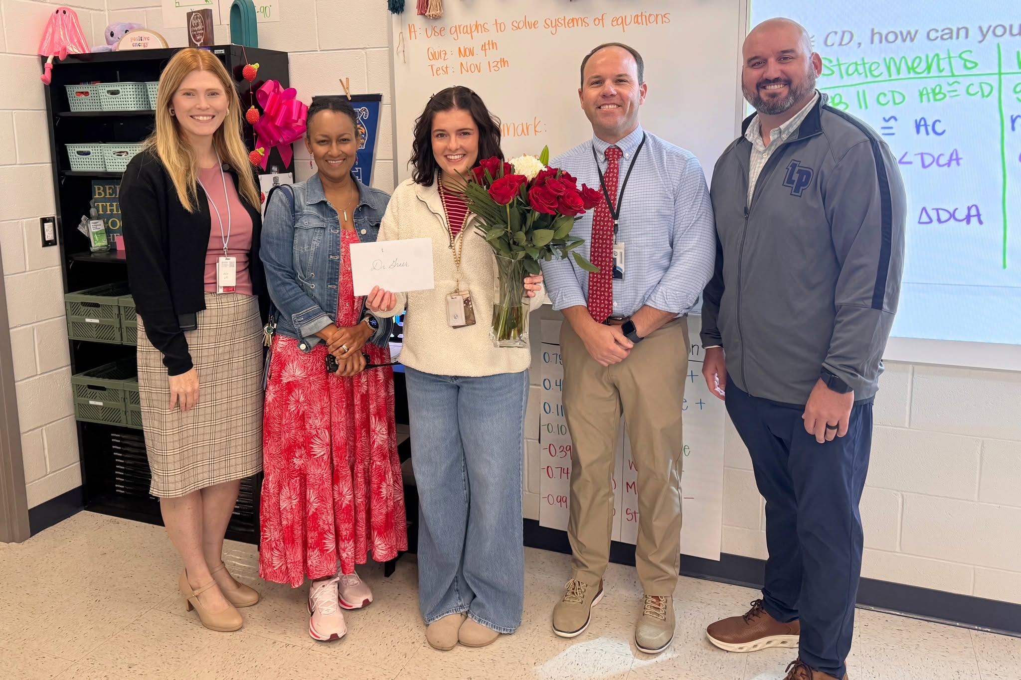 Dr. Casey Greer, center, holds roses and a card while celebrating with four others in her classroom.